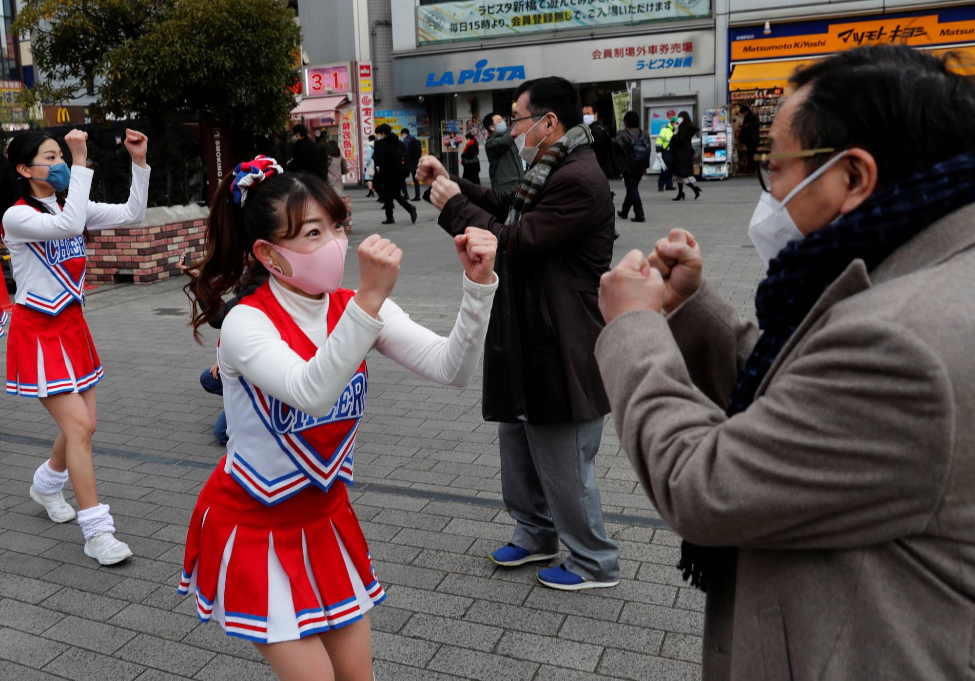 Cheerleaders perform in front of Shimbashi Station during the commuting hour in Tokyo on Thursday. | REUTERS